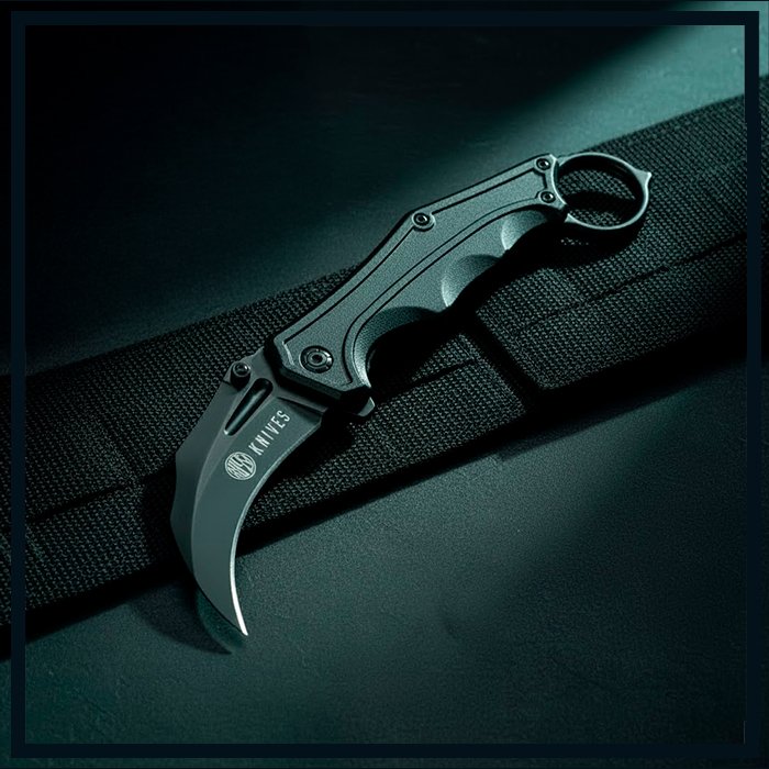 Close-up do canivete Rossi Jibóia tático dobrável, todo preto e fosco, com lâmina curva estilo Karambit e anel de segurança na extremidade do cabo, posicionado sobre uma superfície escura e texturizada.